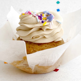 Vegan banana chocolate chip cupcake topped with brown sugar icing and colourful sprinkles.