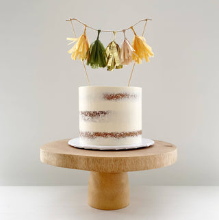 Semi-Naked Cake with a tassel cake topper in orange, green and gold sitting on a wooden cake stand.